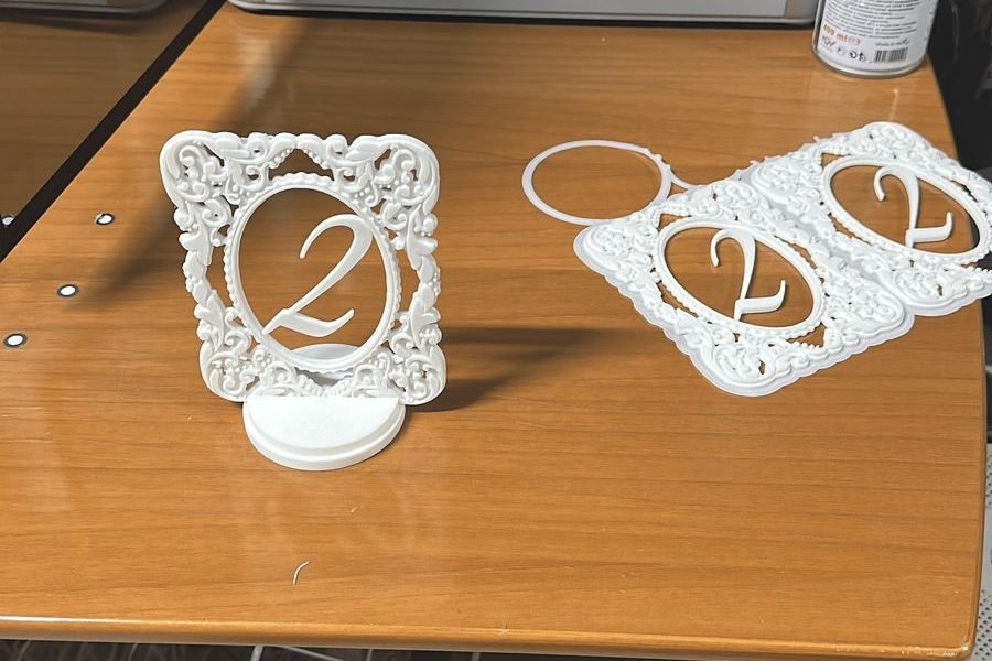 Numere de masă printate 3D din PLA alb, pe o masă din atelier